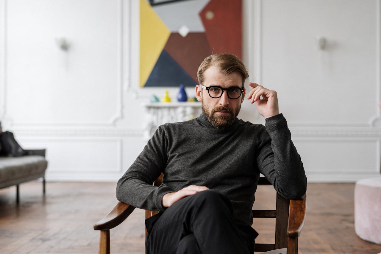 Man with glasses seated in modern interior with abstract art.